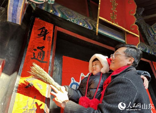 春節(jié)前，孔子后裔在孔府重光門前貼春聯(lián)。 人民網(wǎng) 喬姝攝